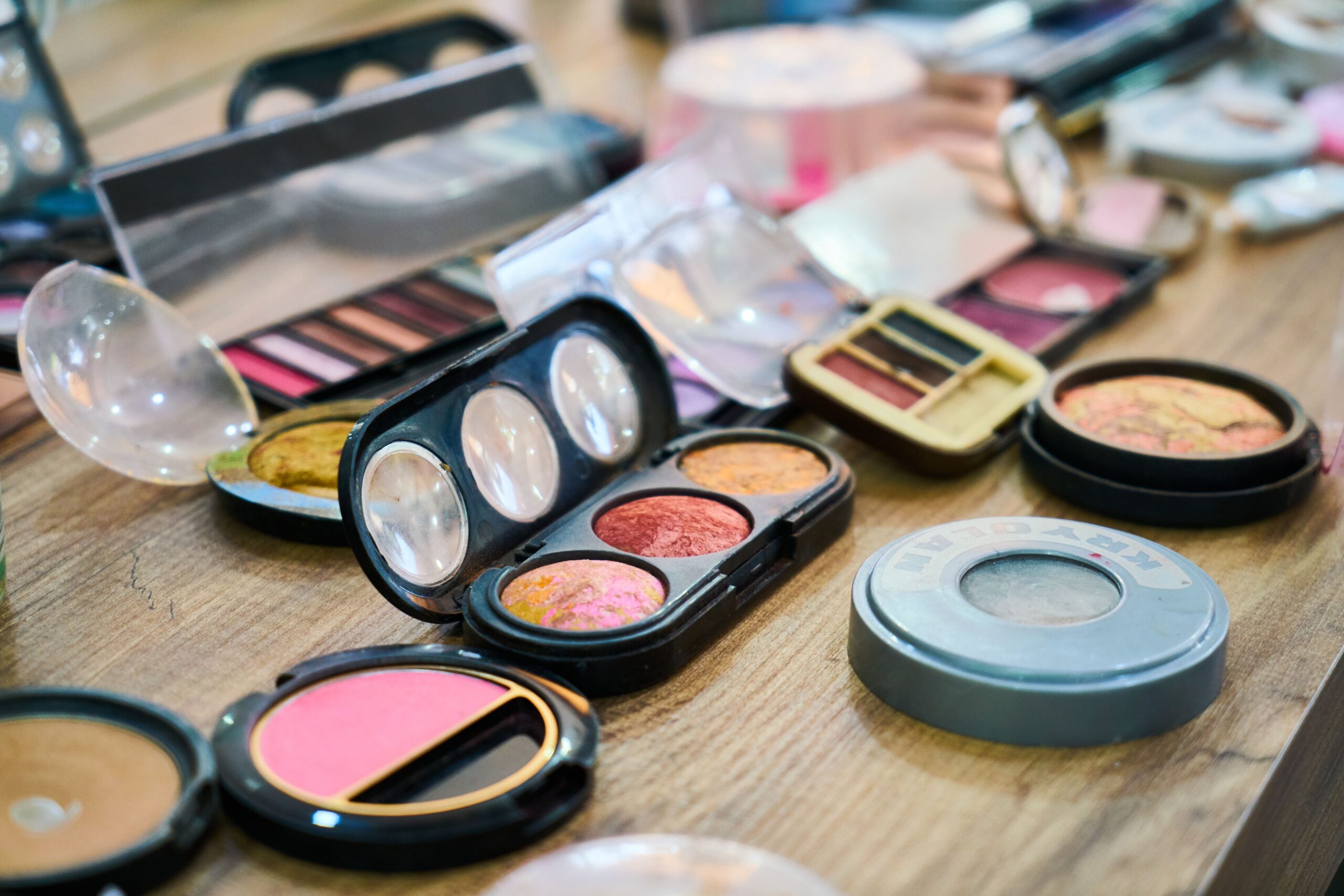 Assorted makeup palettes, blushes, and cosmetic products arranged on a wooden vanity