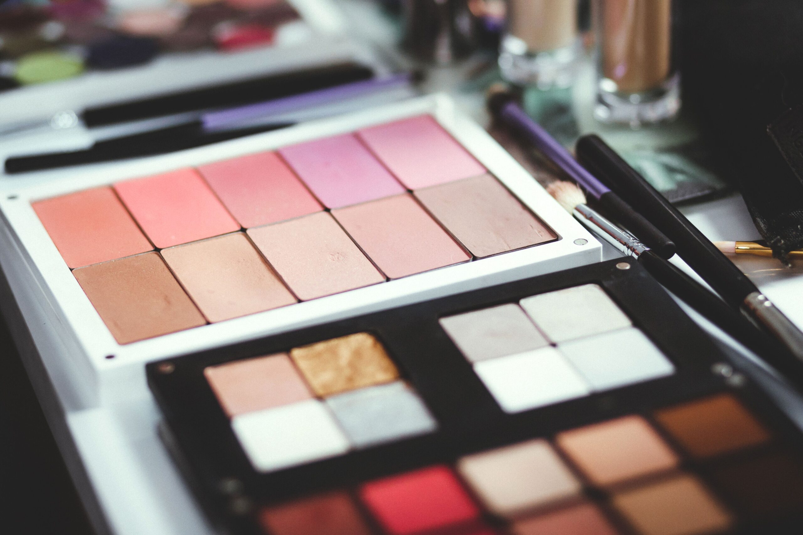 Professional makeup palettes with blush, highlighter, and eyeshadow shades alongside makeup brushes